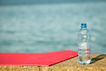 Pink sport mat and water bottle outdoor on sea shore