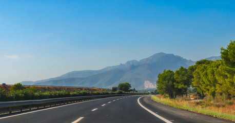 Sunshine on fresh black tarmac on a coastal highway running through the foothills and mountain ranges of continental Europe in Spain.  Road to Madrid. - 103575700