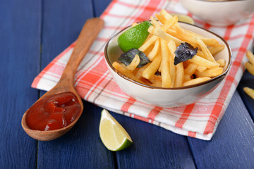 French fried potatoes in bowl with basil and sauce on old wooden background