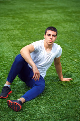 Young smiling sportsman sitting on grass