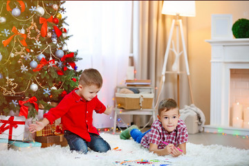 Two cute small brothers playing on Christmas tree background