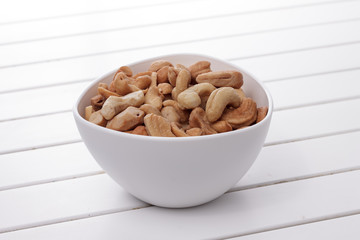 Pile of cashew nuts in a bowl on white wooden table