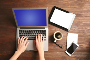 Modern tablet, mobile phone, coffee cup and female hands using laptop, on the wooden background