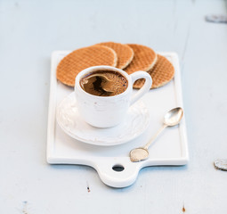 Dutch caramel stroopwafels and cup of black coffee on white ceramic serving board over light blue wooden backdrop