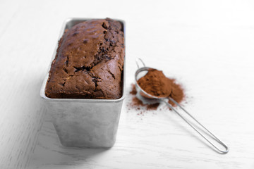 Chocolate cake in baking dish with cocoa powder on white table