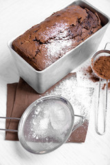 Chocolate cake in baking dish with powdered sugar on white table