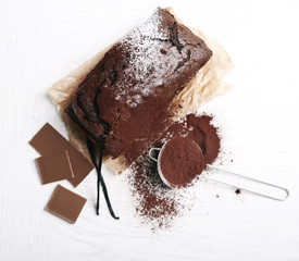 Chocolate cake with cocoa powder, vanilla pods on white table