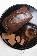 Chocolate cake with icing and cocoa powder on baking dish over white table