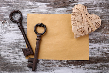 Old key with decorative heart and sheet of paper on grey wooden background, close up