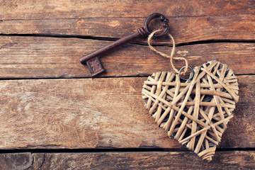 Old key with decorative heart on wooden background, close up