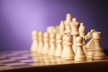 Chess pieces and game board on purple blurred background