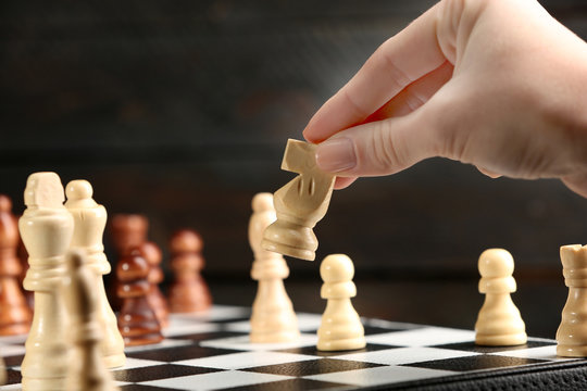 Female hand playing chess on wooden background