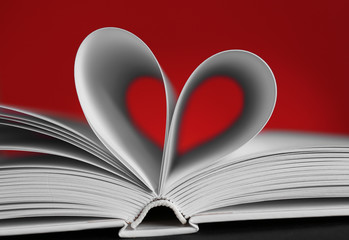Sheets of book curved into heart shape on unfocused red background