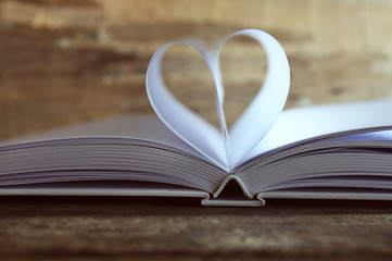 Heart from book pages on wooden blurred background