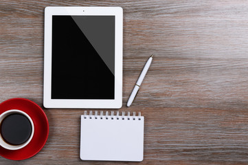 Tablet with cup of coffee and notepad on wooden table