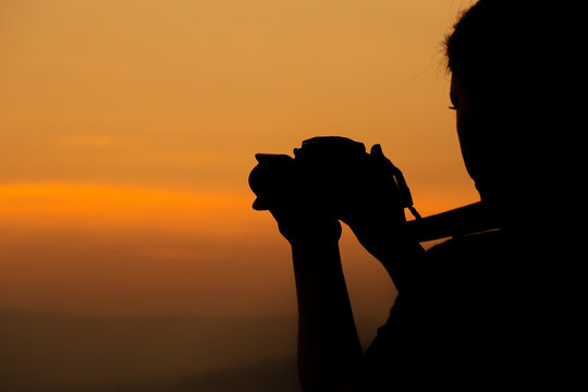 Silhouette of woman shooting with camera at sunset