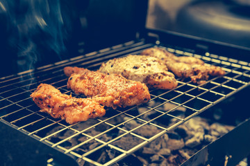 Grilled chicken with black pepper on a barbecue and smoke. Vintage style.