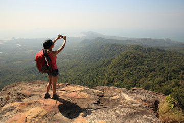 young woman backpacker taking photo with camera on mountain peak