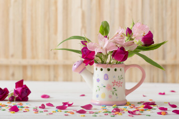 bouquet of bright flowers in watering can on wooden background