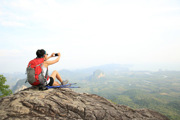young woman backpacker taking photo with cellphone on mountain peak