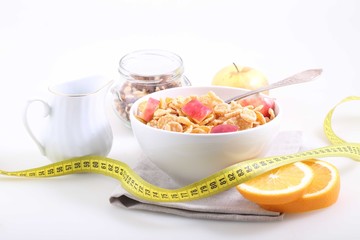 Corn and rice flakes with a fresh apple, an orange and a measuri