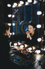 Young beautiful woman applying her make-up lips, looking in a mirror, sitting on chair at Theatre...