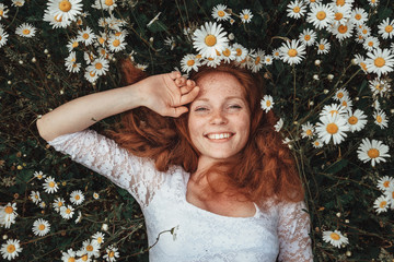 Beautiful young girl with curly red hair in chamomile field - obrazy, fototapety, plakaty