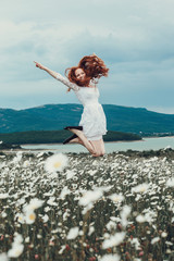 Beautiful young girl with curly red hair in chamomile field