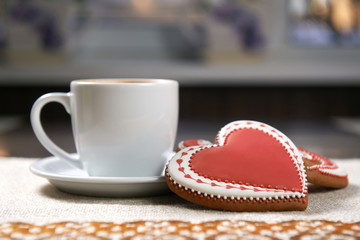 Silent love. Closeup shot of a cup of warming winter beverage and three Valentine’s day decorated cookies on the table
