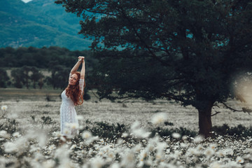 Beautiful young girl with curly red hair in chamomile field