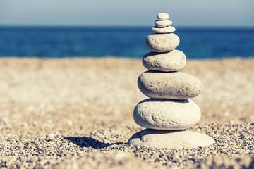 Stones balance, vintage retro instagram like hierarchy stack over blue sea background. Spa or well-being, freedom and stability concept on rocks.