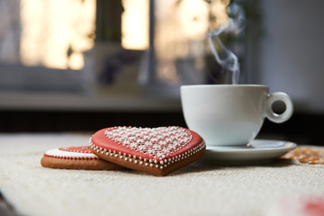 With you in mind. Closeup of a steaming mug of warm beverage and heart shaped Valentine’s day cookies on the table in the kitchen