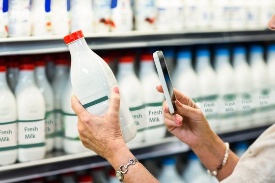 Close Up Of Senior Woman Taking Picture Of Milk Bottle