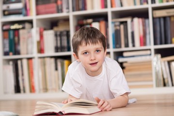 Happy little boy reading a book at home.