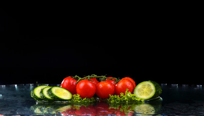 Studio shot with freeze motion of cherry tomatoes and slices of cucumber in water splash on black background
