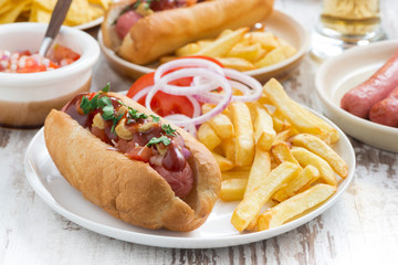 hot dogs with tomatoes, onions and french fries on white table