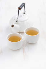 teapot and cups of green tea on a white wooden table, vertical
