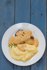 fried meat with sauce and mashed potato on white plate on blue wooden background