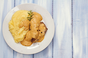 meat with sauce and mashed potato on white plate on blue wooden background