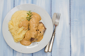 pork with sauce and mashed potato on white plate on blue wooden background