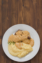 fried meat with sauce and mashed potato on white plate on brown background