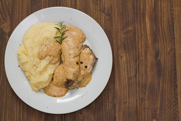 fried meat with sauce and mashed potato on white plate on brown wooden background