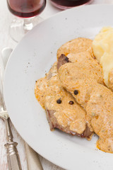 fried meat with sauce and mashed potato on white plate on brown background