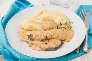 fried pork with sauce and mashed potato on white plate on brown background