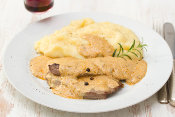 meat with sauce and mashed potato on white plate on brown background