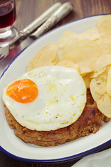 typical portuguese sausage alheira with fried egg and potato on dish on brown wooden background