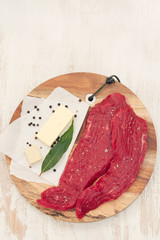 raw beef with butter, herbs and black pepper on wooden board on white wooden background