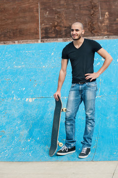Full body portrait of man holding skateboard at skatepark.