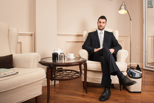 Confident young businessman portrait sit on armchair inside luxury hotel.