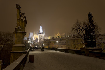Fototapeta na wymiar Night snowy Prague gothic Castle, Bridge Tower and St. Nicholas' Cathedral from Charles Bridge with its Statues, Czech republic